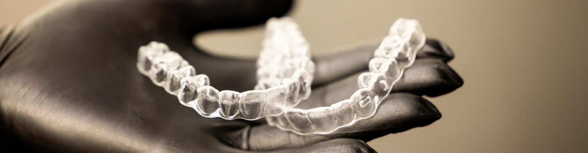 Black-gloved hand holding pair of clear aligners.